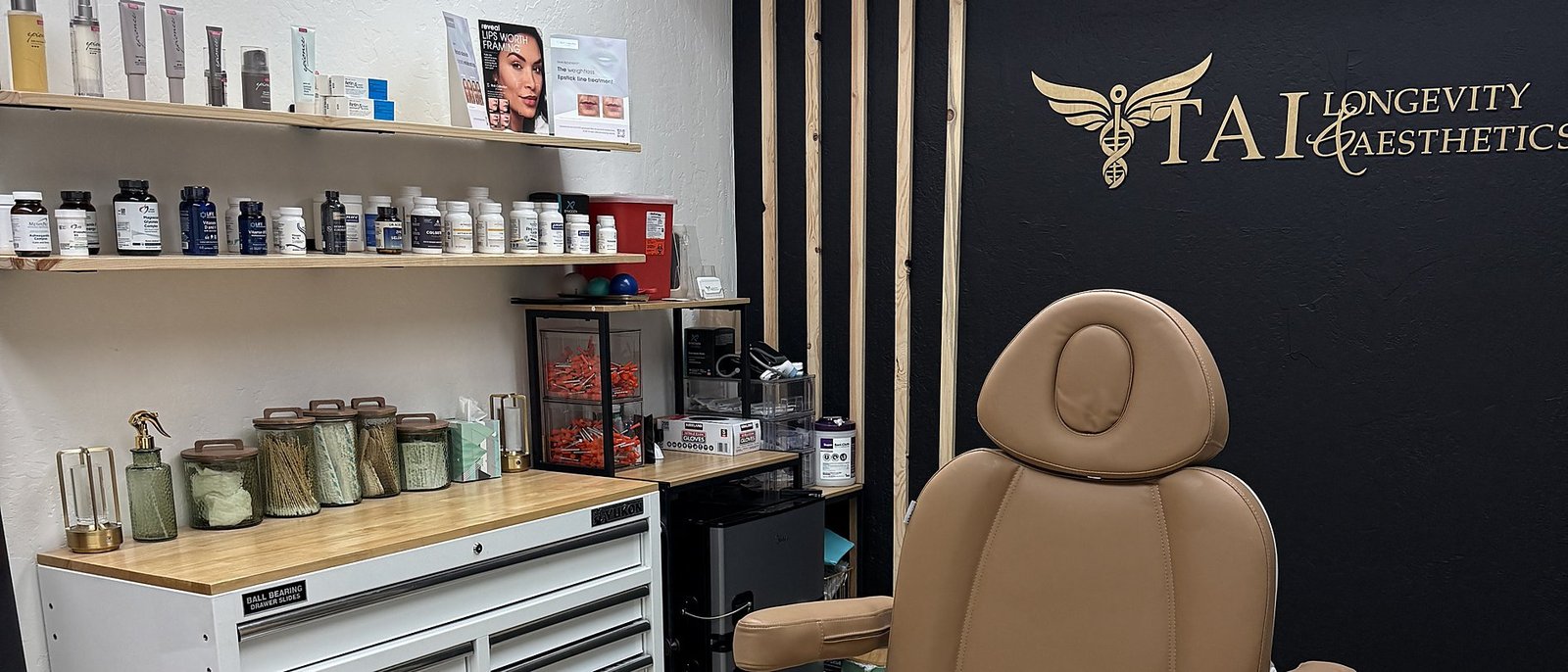 The TAI Longevity & Aesthetics treatment suite — apothecary shelves, medical-grade supplement library, and the signature treatment chair beneath the branded wall.